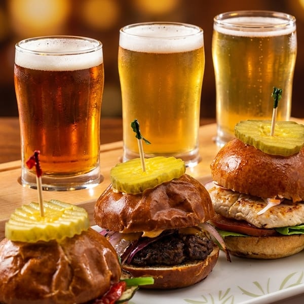 A flight of four beers, from dark to light, with a plate of three gourmet sliders.