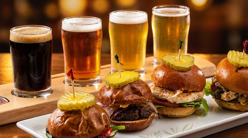 A flight of four beers, from dark to light, with a plate of three gourmet sliders.