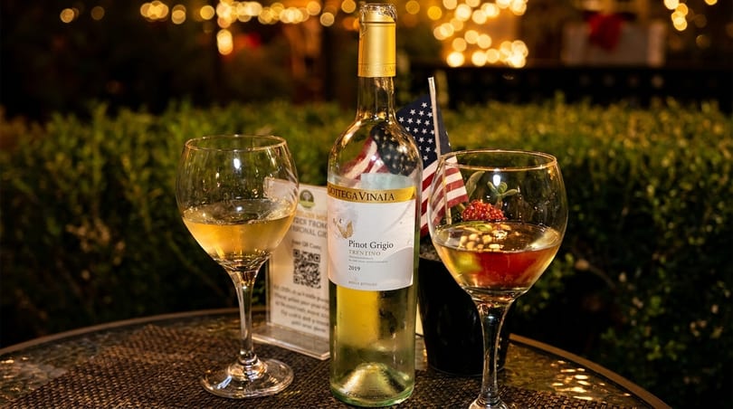 Pinot Grigio wine bottle and two glasses on an outdoor table with an American flag.