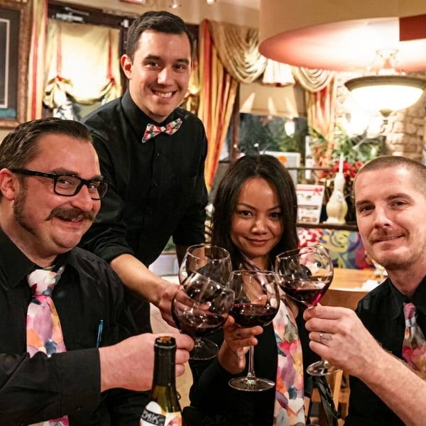 Four restaurant staff members, three men and one woman, toast with red wine glasses in a restaurant.