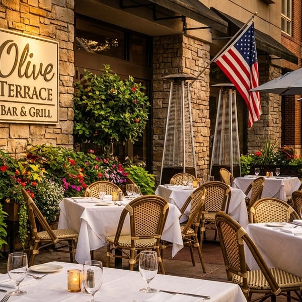 Outdoor dining patio at Olive Terrace Bar & Grill with set tables, umbrellas, and lush flowers.