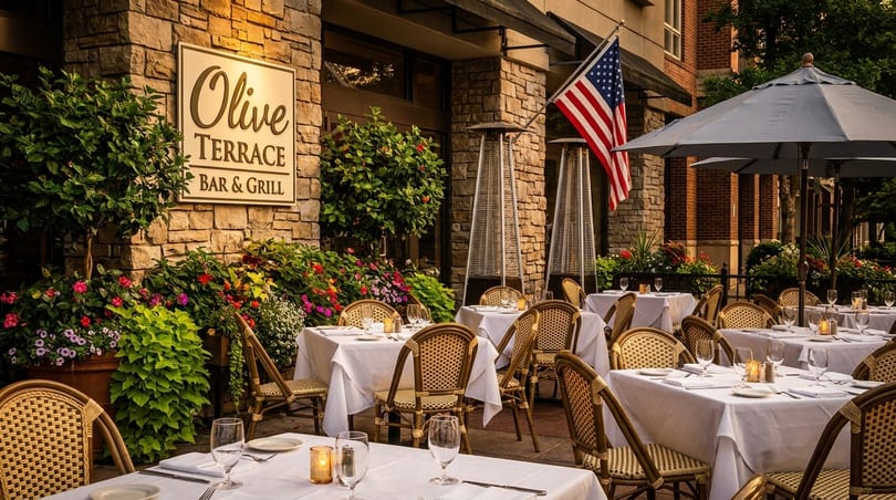 Outdoor dining patio at Olive Terrace Bar & Grill with set tables, umbrellas, and lush flowers.